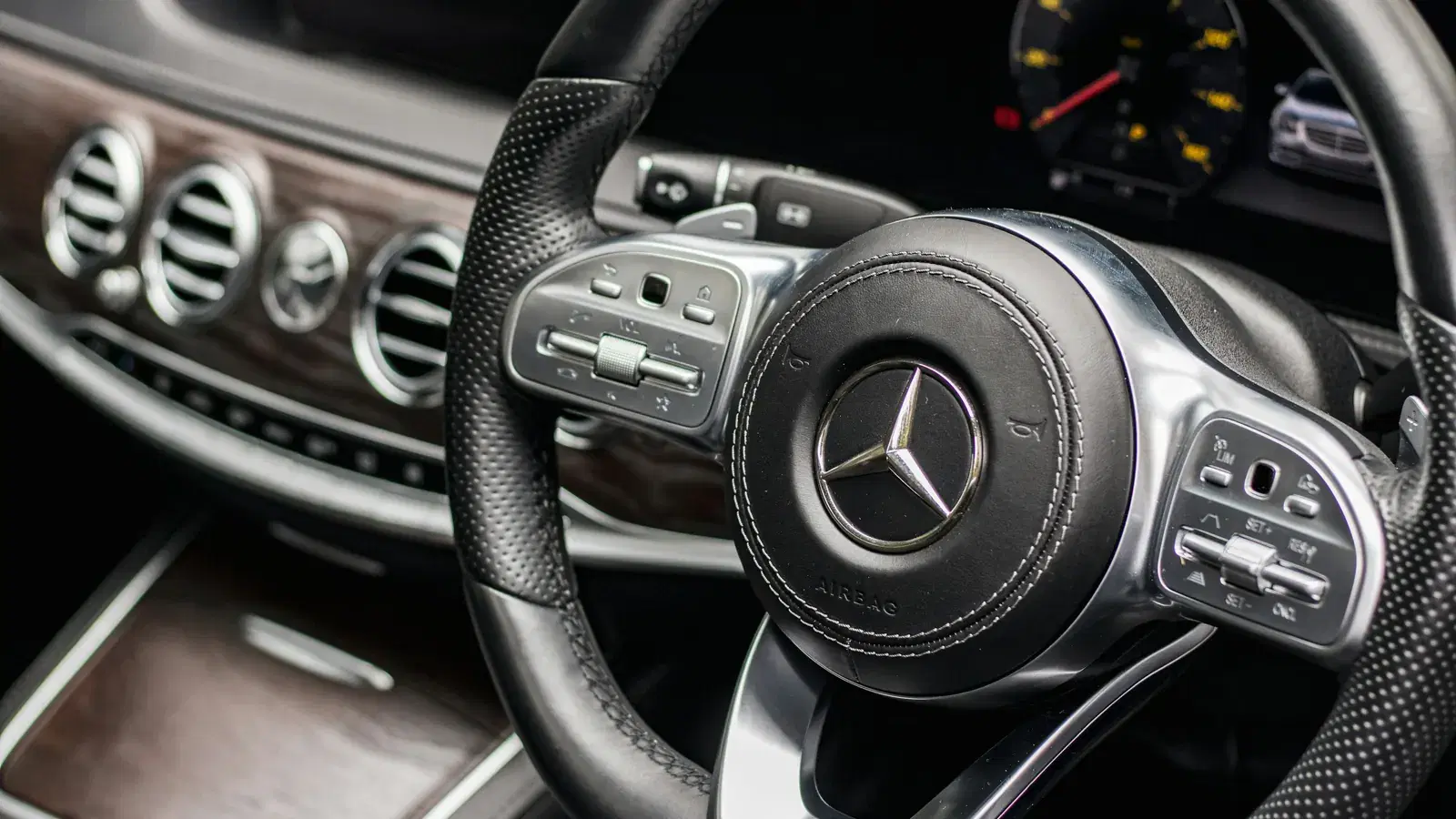 Mercedes-Benz steering wheel with the three-pointed star on the airbag, instrument cluster and wood-trim dash behind