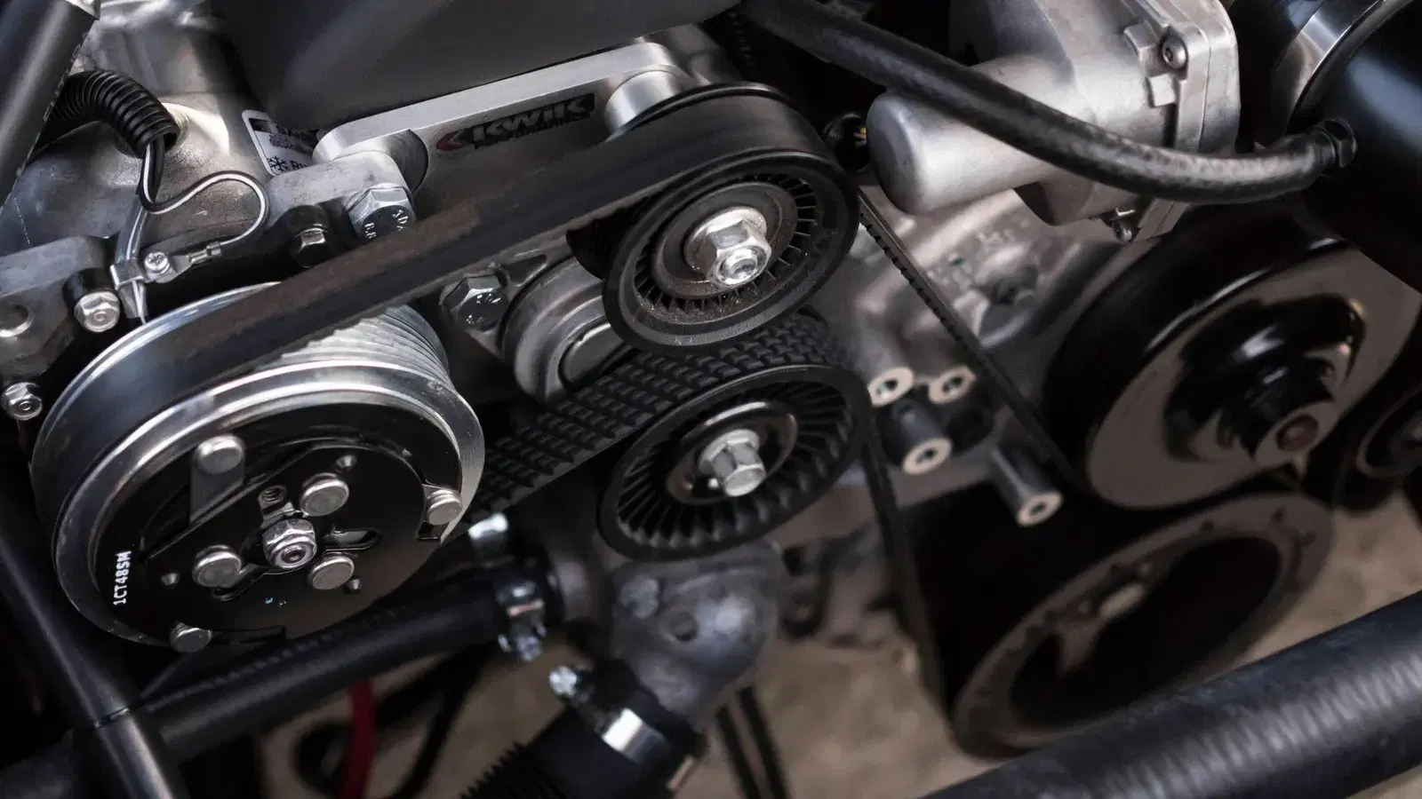 Close-up of an engine's front belt drive, showing belts running over the tensioner and idler pulleys