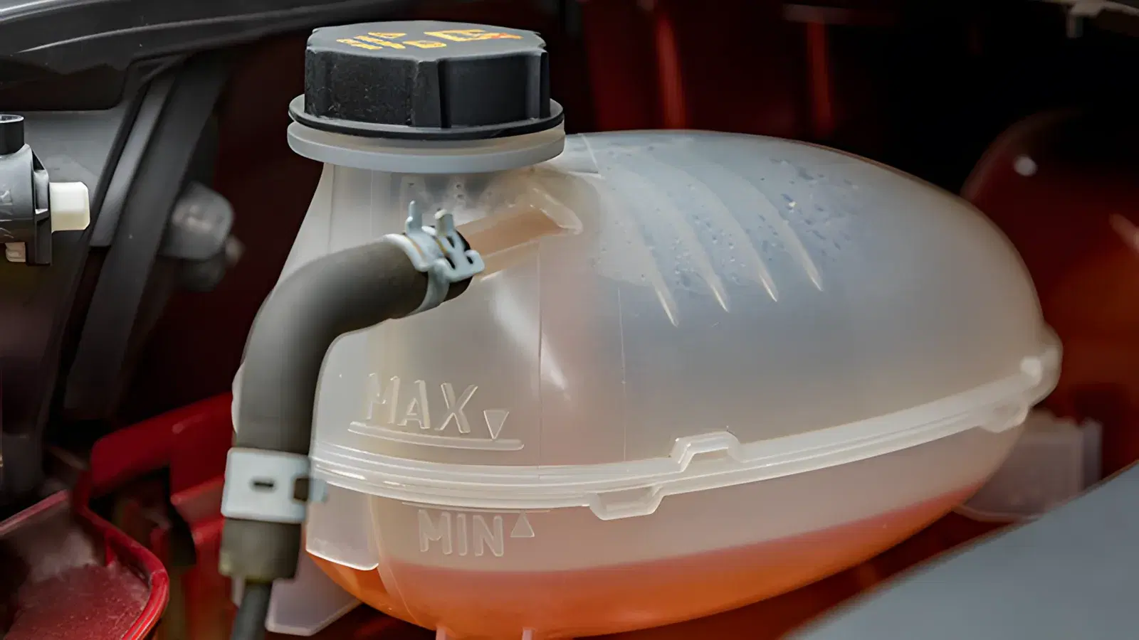 Technician reaching into an engine bay beside a green coolant expansion tank