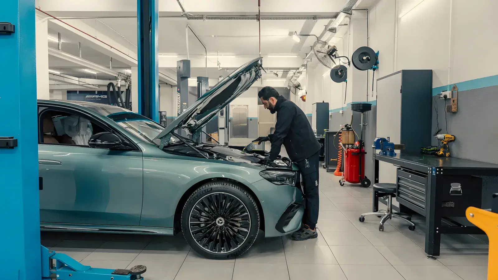 Mechanic leaning into the engine bay of a Mercedes-Benz sedan with its bonnet up in a clean workshop