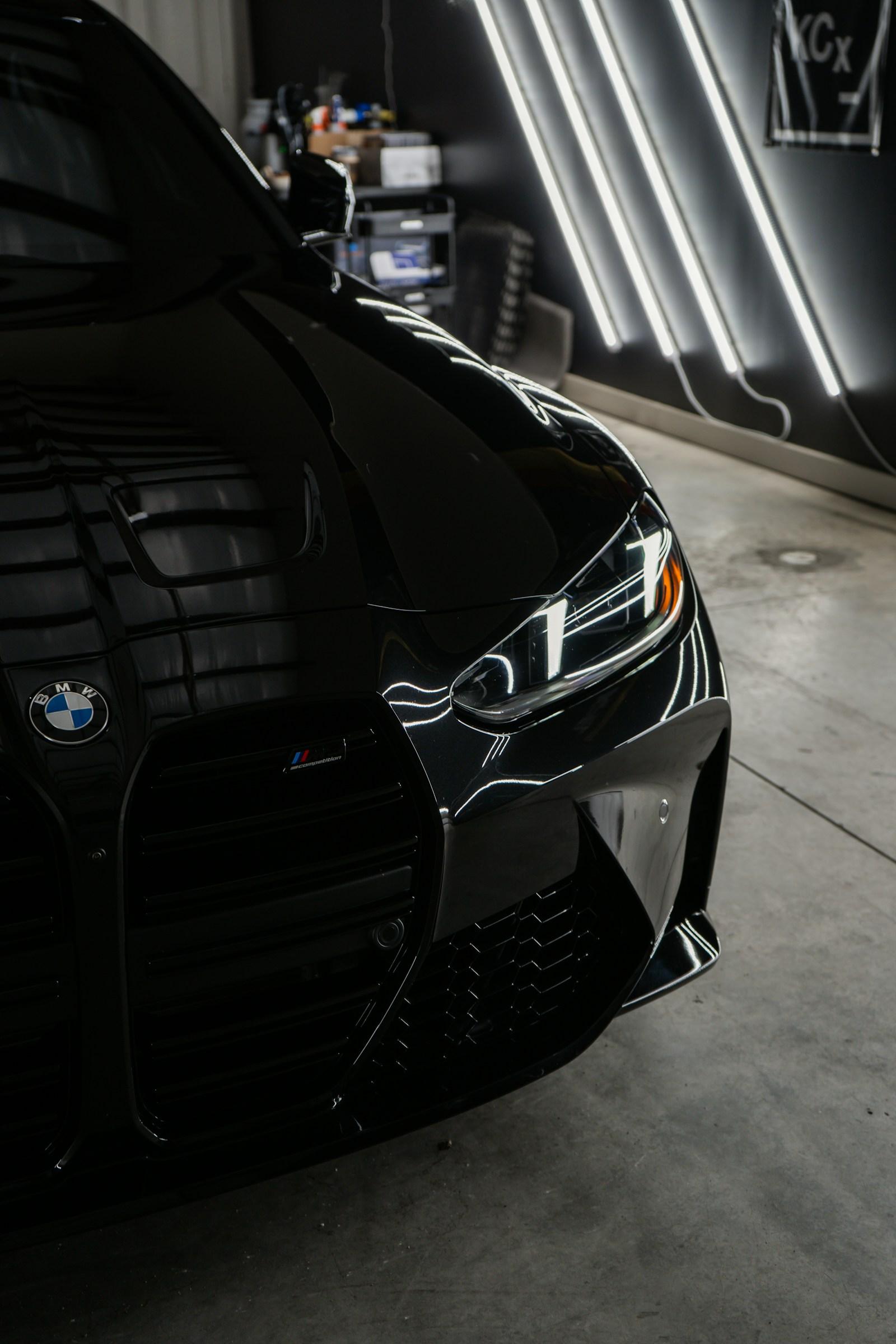 Black BMW M4 front end lit by strip lighting in a dark workshop
