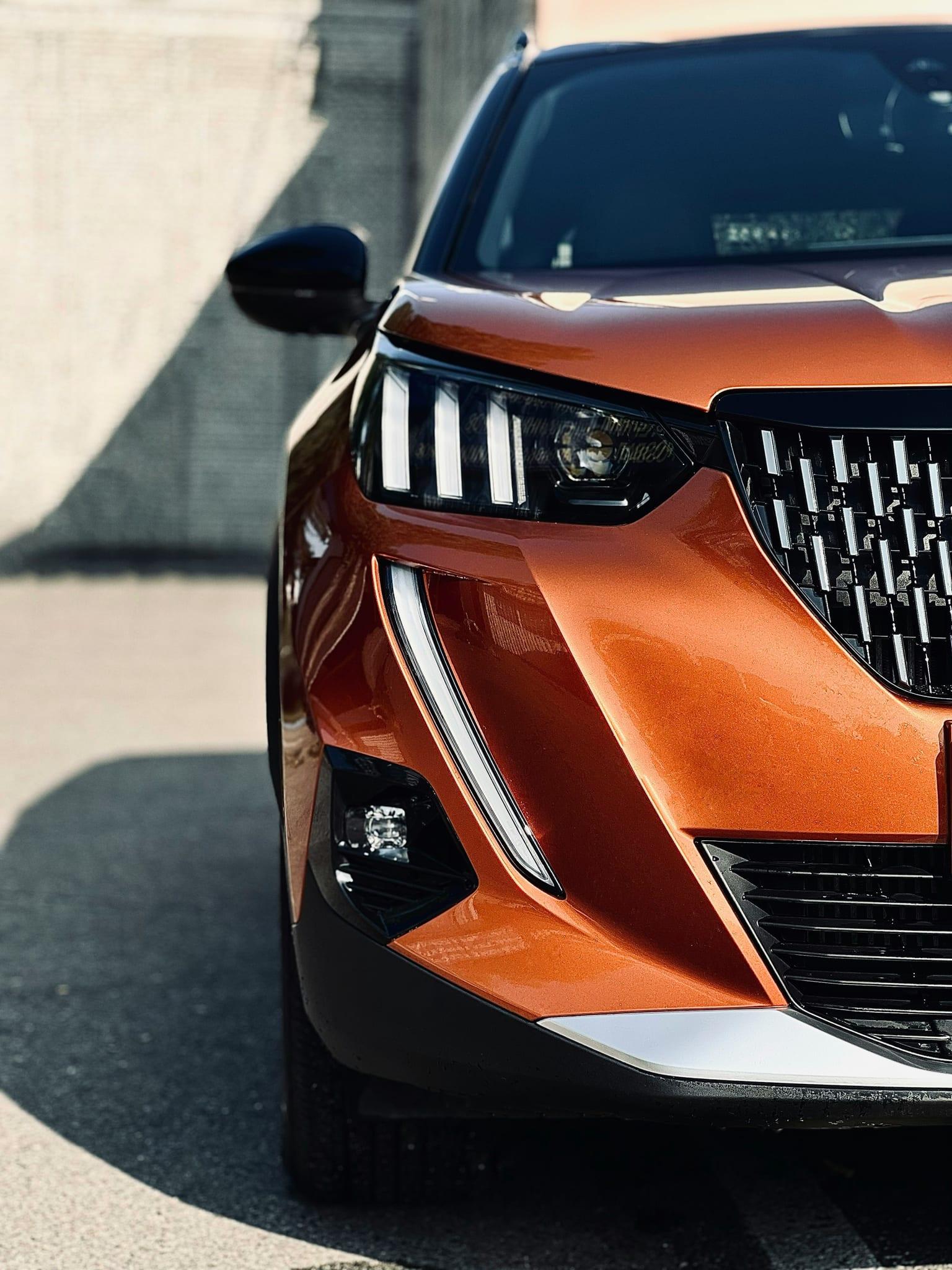 Close-up of the front headlight and grille of an orange Peugeot SUV