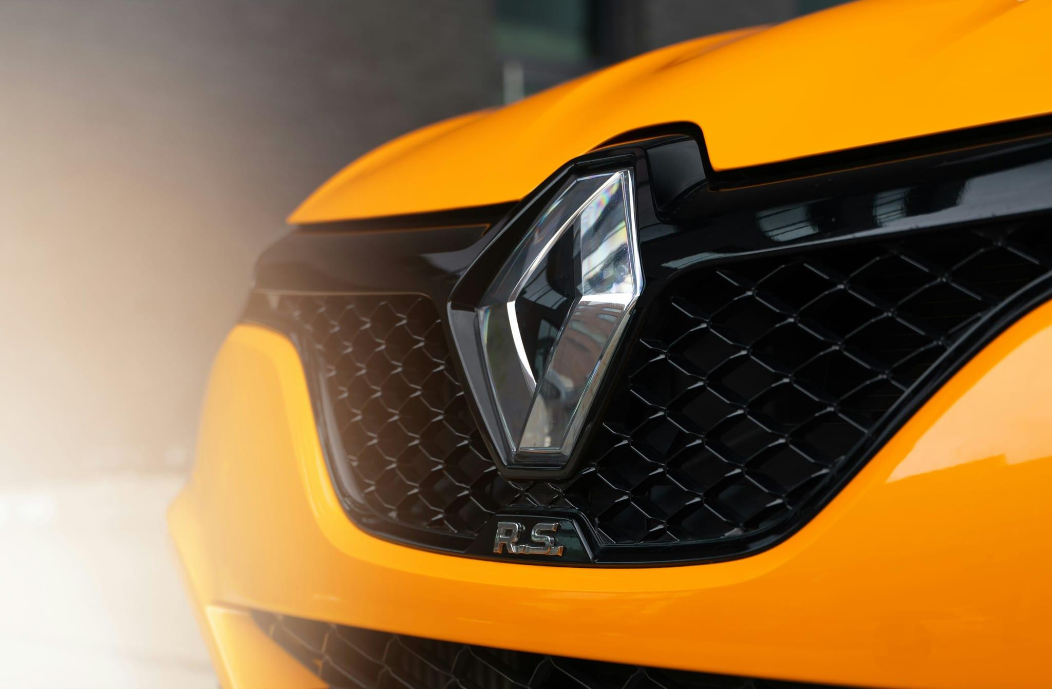 Close-up of the Renault diamond badge on the grille of a yellow R.S. hot hatch