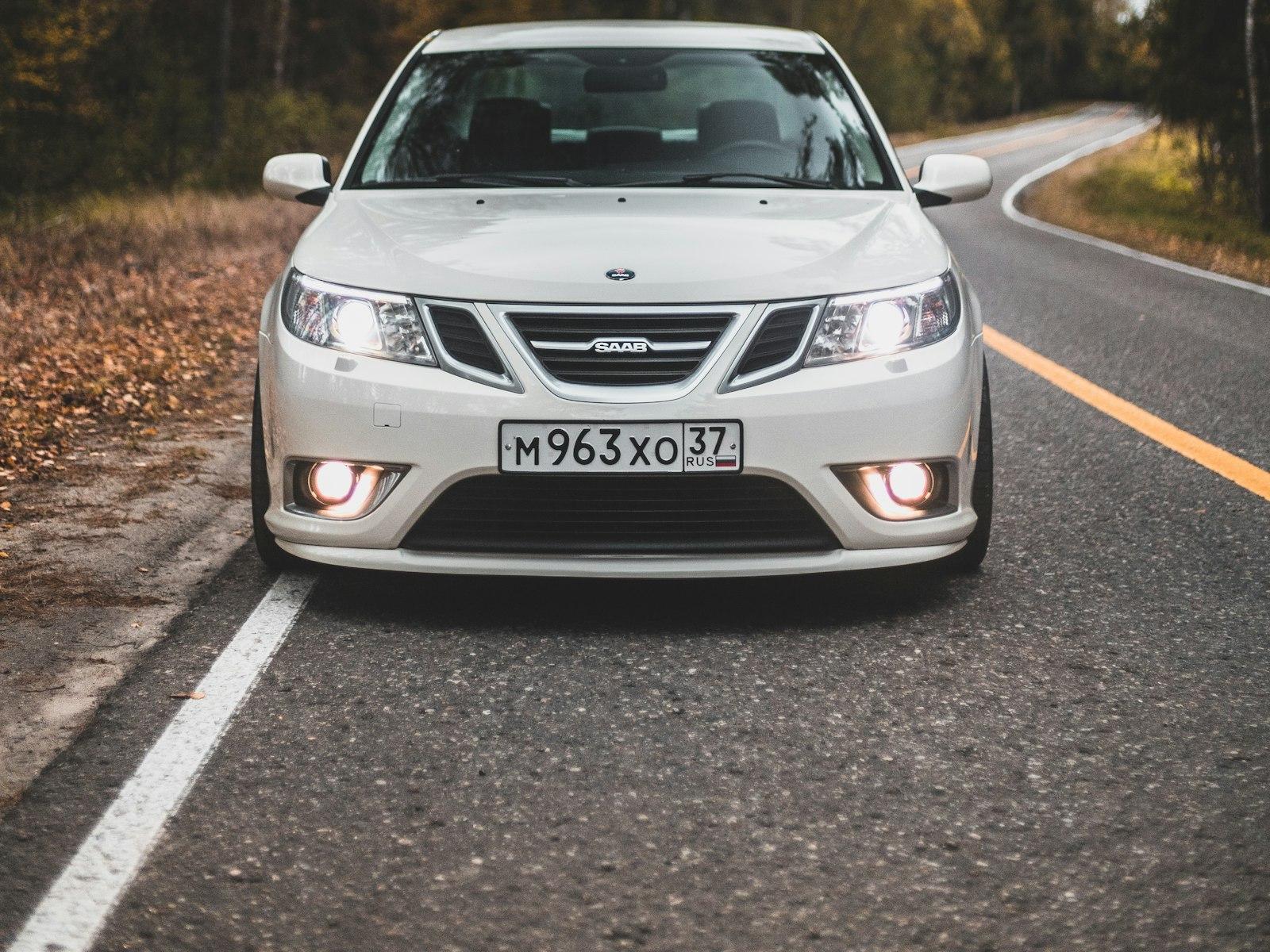 White Saab 9-3 head-on with fog lamps lit on an autumn forest road